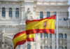 Two Spanish flags waving in front of a historic building