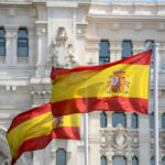 Two Spanish flags waving in front of a historic building