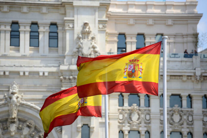 Two Spanish flags waving in front of a historic building