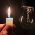 Blackout Fears Surge: AI Centers Threaten Grid A hand holding a lit candle next to a hanging light bulb