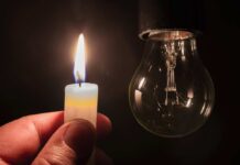 Blackout Fears Surge: AI Centers Threaten Grid A hand holding a lit candle next to a hanging light bulb