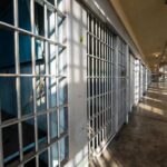 Interior view of a prison corridor with jail cells and sunlight streaming through windows