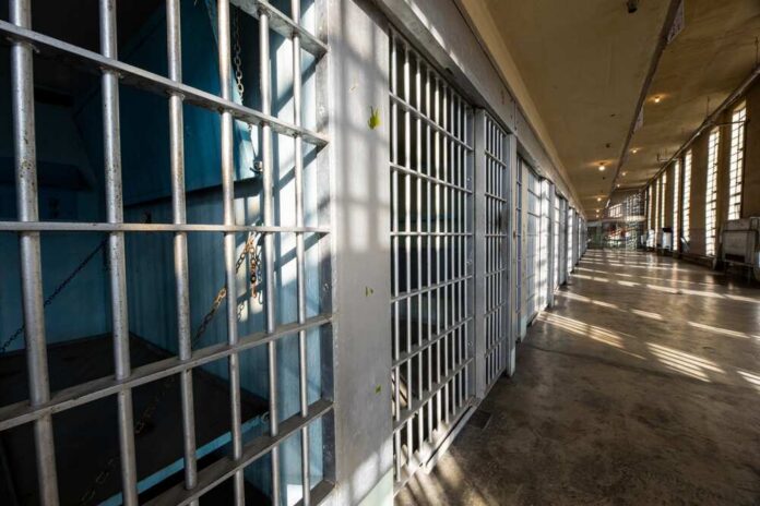 Interior view of a prison corridor with jail cells and sunlight streaming through windows
