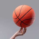 A hand holding an orange basketball against a gray background