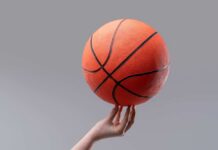A hand holding an orange basketball against a gray background