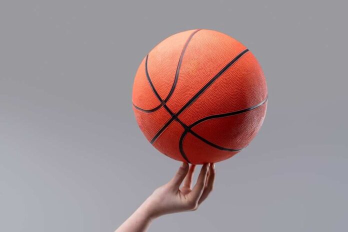 A hand holding an orange basketball against a gray background