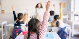 Students in a classroom raising their hands to answer a question