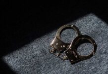 A pair of handcuffs resting on a dark surface with light casting a shadow
