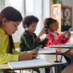 Children in a classroom focused on their smartphones