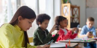 Children in a classroom focused on their smartphones