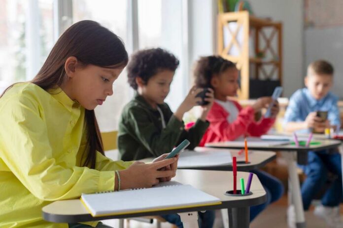 Children in a classroom focused on their smartphones