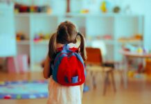 A young child with a red backpack standing in a colorful classroom