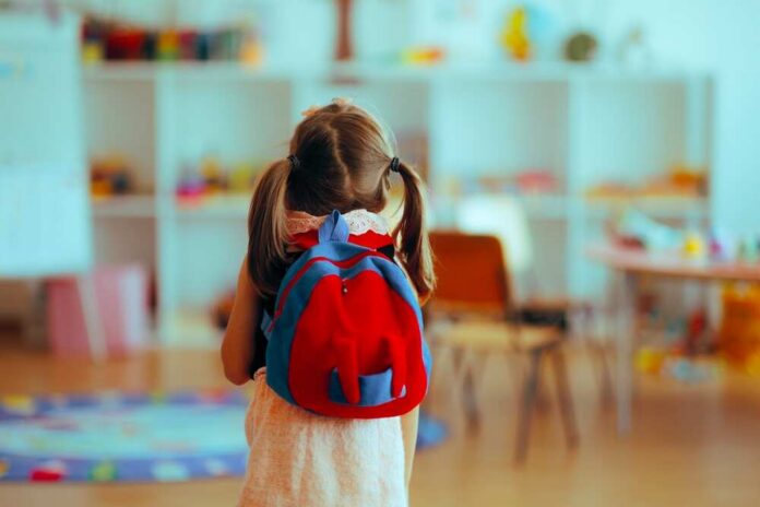 A young child with a red backpack standing in a colorful classroom