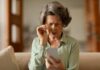 Elderly woman with reading glasses looking surprised while using a smartphone