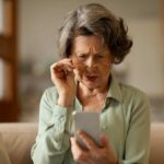 Elderly woman with reading glasses looking surprised while using a smartphone