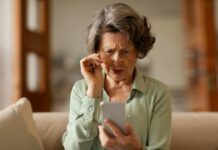 Elderly woman with reading glasses looking surprised while using a smartphone