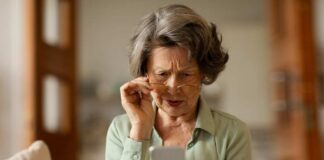 Elderly woman with reading glasses looking surprised while using a smartphone