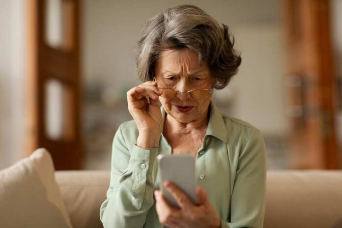 Elderly woman with reading glasses looking surprised while using a smartphone