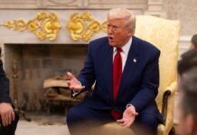 A man in a blue suit and red tie gesturing during a discussion in a formal setting