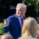 Explosive Allegations: Trump’s Cognitive Fitness Questioned A man in a blue suit and red tie gestures while speaking to a crowd