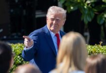 A man in a blue suit and red tie gestures while speaking to a crowd
