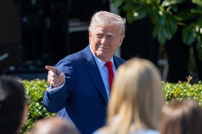 A man in a blue suit and red tie gestures while speaking to a crowd
