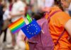 A person with a purple backpack displaying a rainbow flag and an EU flag