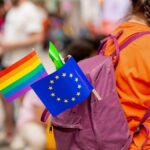 A person with a purple backpack displaying a rainbow flag and an EU flag