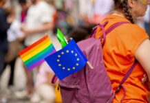 A person with a purple backpack displaying a rainbow flag and an EU flag