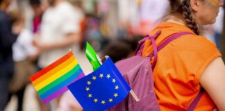 A person with a purple backpack displaying a rainbow flag and an EU flag