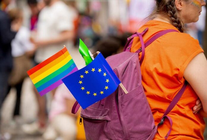 A person with a purple backpack displaying a rainbow flag and an EU flag