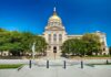 Front view of a government building with a golden dome and surrounding greenery