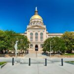 Front view of a government building with a golden dome and surrounding greenery