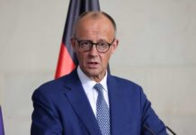 A government official speaking at a press conference with national flags in the background