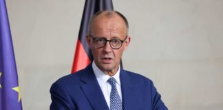A government official speaking at a press conference with national flags in the background