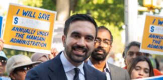A man speaking at a rally with supporters holding protest signs