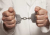 A person in a white coat holding handcuffs tightly