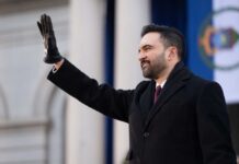 A man in a black coat and gloves waving during a formal event