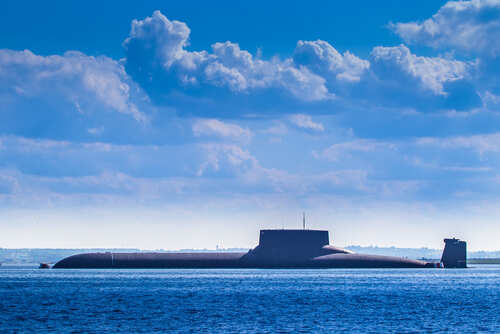 A submarine partially submerged in the ocean under a cloudy sky