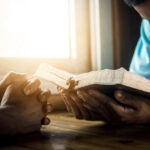 Two individuals engaged in prayer with a Bible