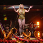 Shocking DUI Arrest: Britney’s Downward Spiral A performer in a gold outfit on stage with dancers in the background