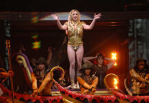 A performer in a gold outfit on stage with dancers in the background