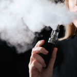Vaping HAZARD: Youth Cancer Cases Surge Person vaping, exhaling thick vapor cloud.