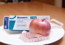Ozempic medication box next to a red apple and measuring tape on a plate