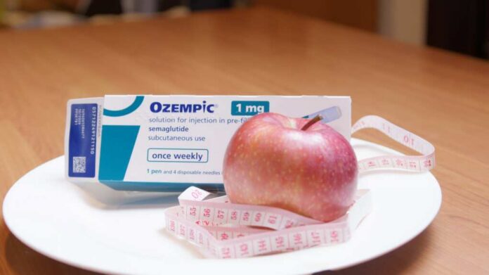 Ozempic medication box next to a red apple and measuring tape on a plate
