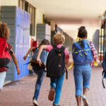 Children with backpacks running in a school corridor