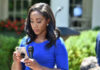 A journalist in a blue dress checking her smartphone at an outdoor press conference