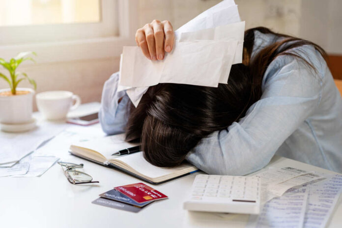 Person with head down on a desk surrounded by paperwork and a calculator