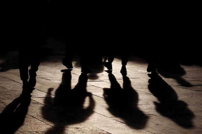 shutterstock_2026715138.jpg Silhouettes of people walking, casting shadows on the ground