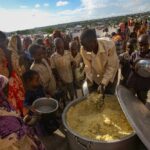 Children and adults gathered around a large pot of food during a distribution event